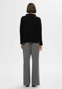Pull en maille noir avec un col montant, texture côtelée et épaules tombantes, associé à un pantalon large gris.