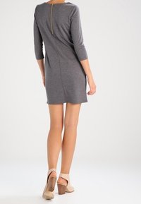 Grå klänning med trekvartslång ärm och dragkedja i ryggen, tillverkad av ett slätt material, knälång, matchad med beige klackar med kraftig klack.