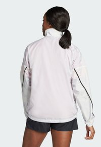 Giacca leggera rosa chiaro con maniche lunghe, colletto alto, polsini elastici e dettagli neri sulle maniche. Materiale liscio e resistente all'acqua.