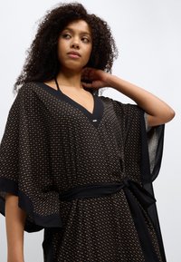 Vêtement style kimono noir avec un col en V, des motifs géométriques complexes en or, et une taille ceinturée. Tissu fluide avec de larges manches.