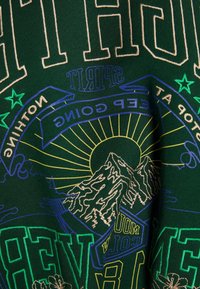 Mörkgrön skjorta med intrikata flerf ärgade broderier. Designen inkluderar berg, stjärnor och text med gula och blå accenter.