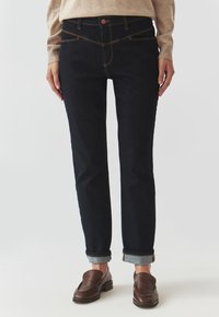Jeans din denim închis, cu o croială slim, design cu cinci buzunare, manșete rulouri și cusături contrastante. Purtați cu un pulover tricotat bej și pantofi maro.