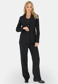 Granatowy garnitur w prążki z dopasowaną marynarką, dwiema kieszeniami i czarnymi guzikami; zestawiony z szerokimi spodniami i błyszczącymi czarnymi butami.