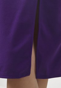 Gros plan sur une jupe violette avec une fente avant dévoilant des jambes nues en dessous.