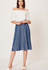 Biała bluzka na ramiączkach z dekoltem typu off-shoulder, w paski, zestawiona z niebieską spódnicą długą do kolan z denimu. Proste detale z guzikami i gładkie wykończenie materiału.