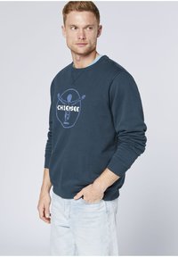 Navy blue sweatshirt with a round graphic print, featuring an abstract figure and text. Cotton blend fabric with ribbed cuffs and neckline.