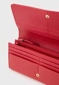 Κόκκινο πορτοφόλι κατασκευασμένο από υφασμένο δέρμα με λείο εσωτερικό. Διαθέτει πολλαπλές θήκες για κάρτες, μια θήκη με φερμουάρ και κούμπωμα με χρυσό κλιπ.