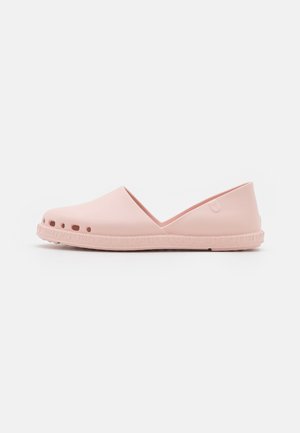 Chaussure légère rose clair à enfiler avec des trous de ventilation près de la semelle et une semelle en caoutchouc texturée, vue de côté sur fond blanc.
