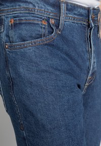 Jeans in denim blu con un design aderente, caratterizzati da cuciture arancioni a contrasto e tasche frontali e posteriori classiche.