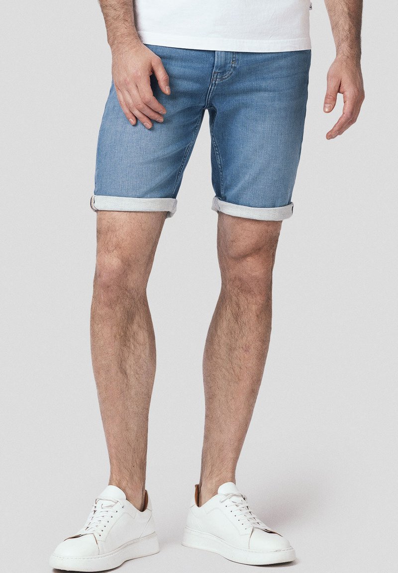 Jasnoniebieskie szorty dżinsowe z podwiniętymi nogawkami, charakteryzujące się klasycznym pięciokieszeniowym wzornictwem. W połączeniu z białymi trampkami, skupiają się na komforcie.