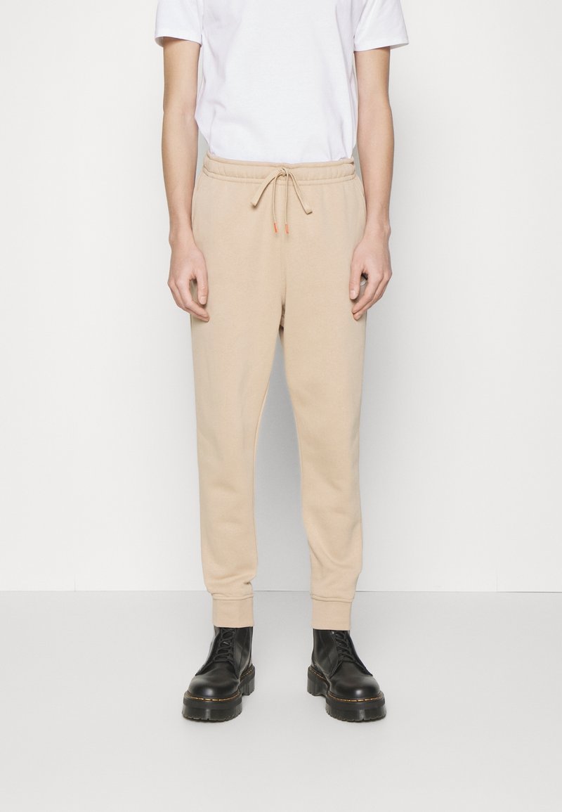 Beige sweatpants met een elastische tailleband en trekkoord, met taps toelopende benen en ribgebreide boorden, gedragen met zwarte veterschoenen.