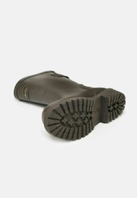 Tmavo khaki gumová členková topánka s textúrovanou podrážkou, bočným zipsom a malou nášivkou pri členku. Má dizajn so zaoblenou špičkou.