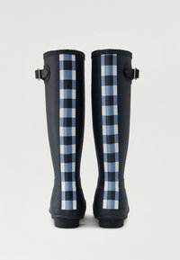 Botas de lluvia de goma negras con rayas a cuadros azules y blancas en los costados, con un detalle de hebilla cerca de la parte superior.