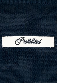 Tissu tricoté bleu foncé avec une étiquette rectangulaire blanche présentant un texte en cursive noire indiquant "Prohibited."