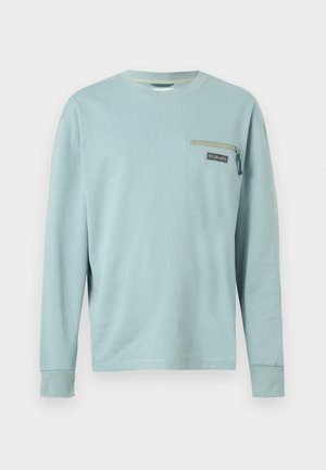 Chemise bleu clair à manches longues avec un petit poche zippée et le logo Columbia sur le côté gauche de la poitrine.