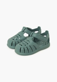 Infradito in plastica verde con design a strisce, lati aperti e chiusura in velcro. Superficie testurizzata con motivi intagliati per la traspirabilità.