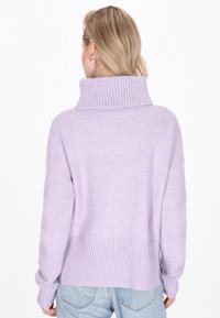 Pulover în nuanță de liliac, realizat dintr-un tricot moale, cu un guler înalt și un tiv ribetat. Prezintă umeri lăsați și mâneci lungi, într-o croială lejeră.