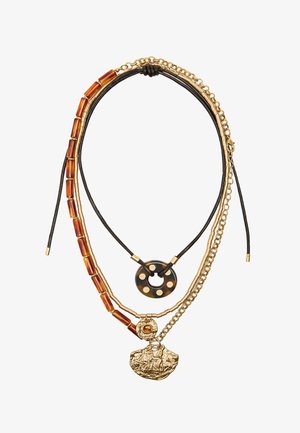 Naszyjnik warstwowy z łańcuszkami w kolorze złotym, teksturowanymi bursztynowymi koralikami oraz okrągłą czarną zawieszką z otworami, a także złotym przywieszką z detalicznym wzorem.