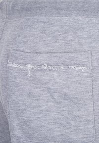 Šedé bavlněné tepláky s kapsou na zadní straně, s třepenými okraji podél švu kapsy. Hladká textura, neformální design.