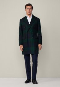 Dvojradový kabát v tmavozelenej a námorníckej kárované vlne, so plochými vreckami, klopami a prispôsobeným strihom. Ploché nohavice a topánky.