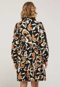 Robe noire avec un motif abstrait audacieux en orange et crème, manches longues bouffantes, taille ajustée et design de jupe en couches. Tissu au toucher doux.