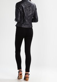 Zwart leren jack met een getailleerd ontwerp, schoudernaden en geribbelde accenten, gedragen over zwarte skinny jeans en gehakte sandalen met enkelbandjes.