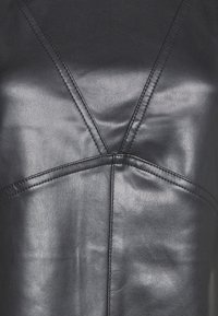 Czarna skóra syntetyczna o gładkiej fakturze, z pionowymi i ukośnymi szwami, które tworzą dynamiczne kształty i strukturę.