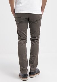 Schmal geschnittene, dunkelolivgrüne Baumwollhose mit glatter Textur, kombiniert mit schwarzen Lederschuhen und einem weißen T-Shirt.