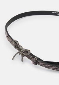 Svart belte med en teksturert rem prydet med sølv rhinestones, fullført med en metallbueformet lås i midten.