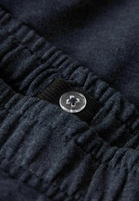 Tessuto blu scuro con una texture a coste e una vita elastica, con un bottone trasparente sul davanti e una striscia nera decorativa.