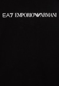 Camiseta de algodón negra con texto del logo blanco "EA7 EMPORIO ARMANI". Textura suave con un diseño clásico de cuello redondo.