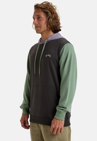 Sudadera con capucha en gris oscuro con mangas verdes. Presenta un forro de capucha morado, un bolsillo frontal y un logo bordado en blanco.