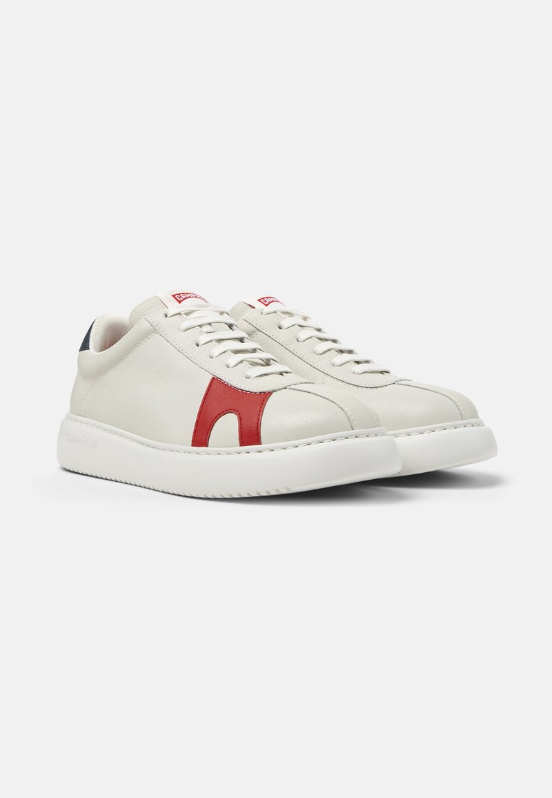 White leather sneakers with red side accents, white laces, cushioned sole, and navy blue heel detail displayed against a plain background.