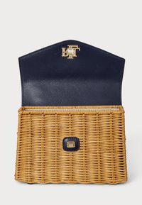 Torba od pletene slame s mornarsko plavim kožnim preklopom, zlatnim logotipom i kvadratnim kopčanjem. Teksturirana površina, strukturirani oblik.