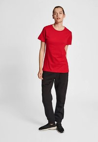 Czerwona koszulka z krótkim rękawem wykonana z bawełny, z okrągłym dekoltem i dopasowanym krojem, zestawiona z luźnymi czarnymi spodniami i czarnymi trampkami.