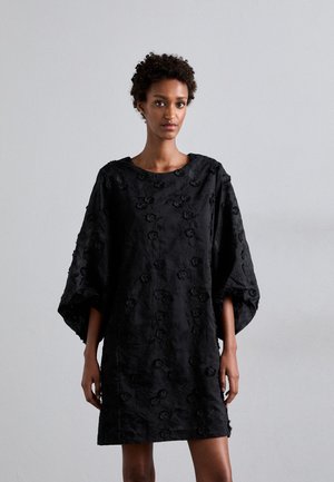 Robe noire à manches larges, texture florale et coupe ample. Dotée d'un col rond et d'une longueur mi-cuisse. Tissu léger.
