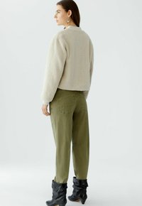 Crème kleurige fleecejas met een boxy fit, gecombineerd met olijf groene broek. Het model draagt zwarte slouchy laarzen en statement oorbellen.