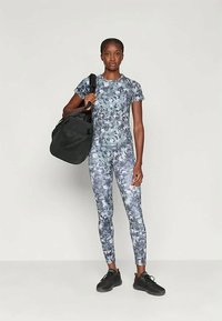 Σετ αθλητικών ρούχων παραλλαγής σε αποχρώσεις του γκρι, με εφαρμοστή κοντομάνικη μπλούζα και κολάν, συνδυασμένα με μια μαύρη τσάντα σέλας και μαύρα αθλητικά παπούτσια.