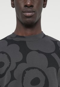 Γκρι πουλόβερ με λουλουδάτο μοτίβο σε σκούρες αποχρώσεις, με ριμπ λαιμόκοψη και λεία υφή. Το σχέδιο καλύπτει ολόκληρο το ύφασμα.