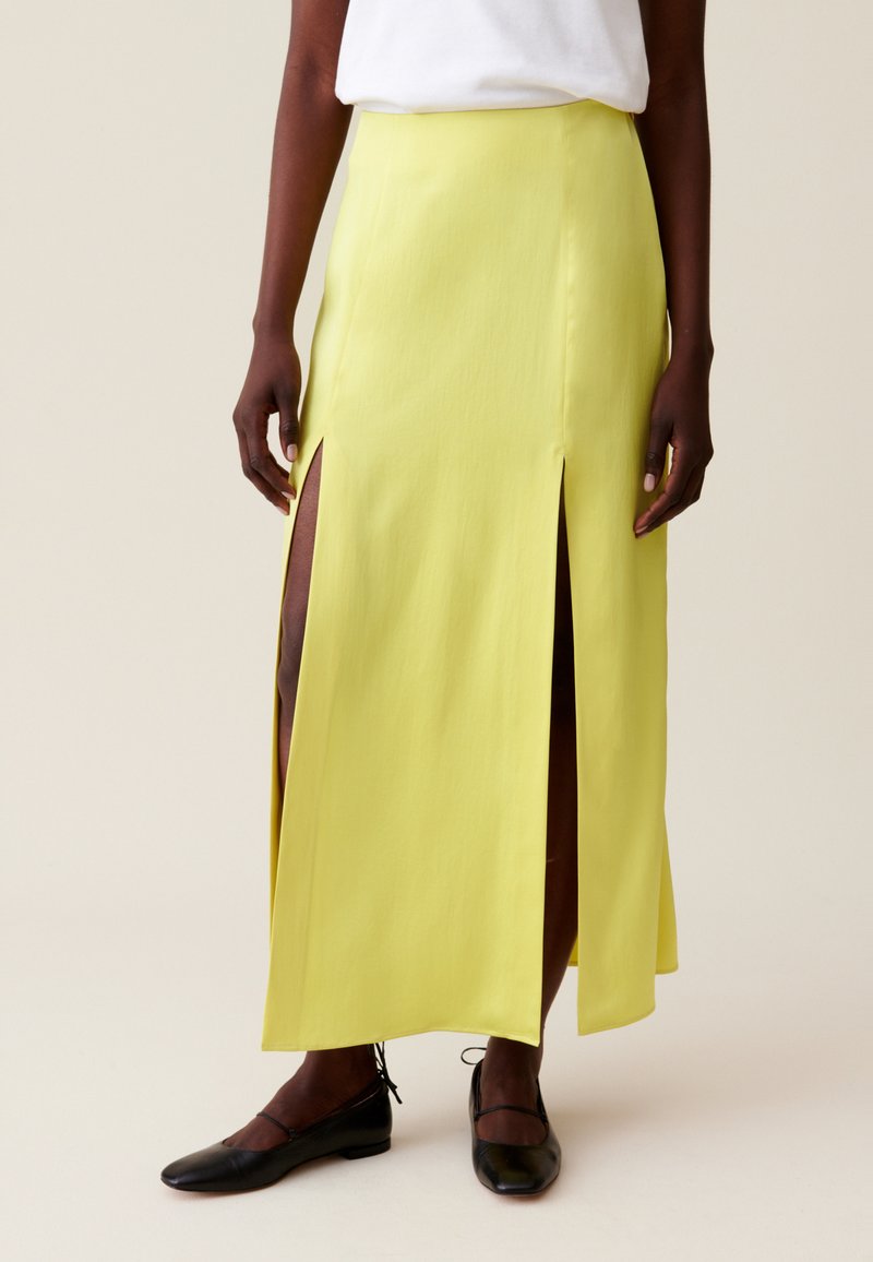 Gonna maxi gialla con due spacchi laterali, texture liscia e design dritto. Abbinata a scarpe nere piatte.