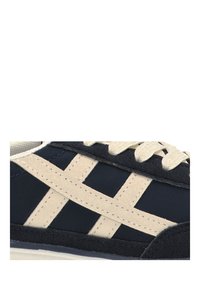 Zapatilla deportiva con parte superior en azul marino, rayas crema, acentos de ante texturizado y cordones blancos. Costuras detalladas visibles en el diseño.
