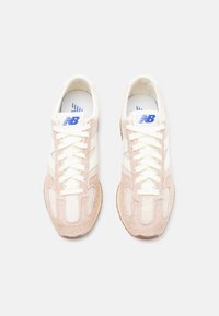 Light pink suede and cream canvas sneakers with white laces, blue logo, and textured accents. Flat beige rubber sole.