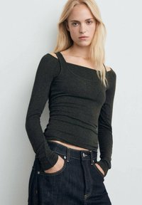Haut à manches longues vert foncé avec un col carré et une coupe ajustée, fabriqué dans un tissu doux. Associé à un jean en denim sombre taille haute.