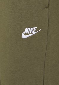 Witte geborduurde Nike-logo op olijfgroene stof, met een deel van een kledingstuk waar de zichtbare stiknaden te zien zijn.