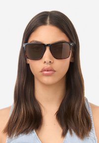 Juodi ir vėžlio kiauto rašto akinukai nuo saulės su tamsiais lęšiais, kvadratiniu rėmeliu, metaliniais akcentais ir blizgiu paviršiumi.