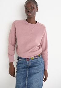 Sweatshirt rose avec un col rond côtelé et des manches longues, associé à une jupe en denim avec une taille ornée de motifs floraux et une légère forme en A.