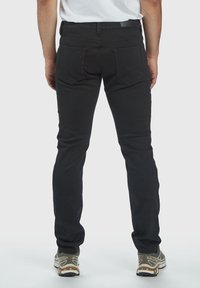 Jeans in denim nero con una vestibilità slim, cinque tasche e cuciture a contrasto. Presentano una texture liscia e un'etichetta in pelle sulla cintura.