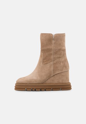 Beige ruskindsankelstøvle med kilehæl og tyk riflet gummisål på ensartet lys baggrund.