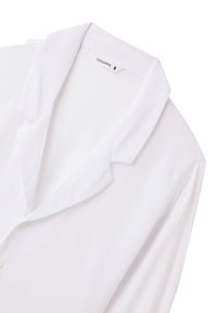 Camicia bianca con colletto, chiusura a bottoni, tessuto leggero, maniche leggermente drappeggiate e un'etichetta con scritto "Terranova S."