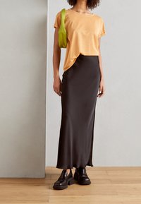 Oranje top met korte mouwen, zwarte satijnen maxi rok en chunky zwarte schoenen. Groene tas die van de schouder hangt. Glad textuur, moderne silhouet.